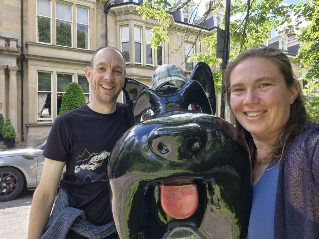 Two people standing smiling on either side of large Scottie sculpture