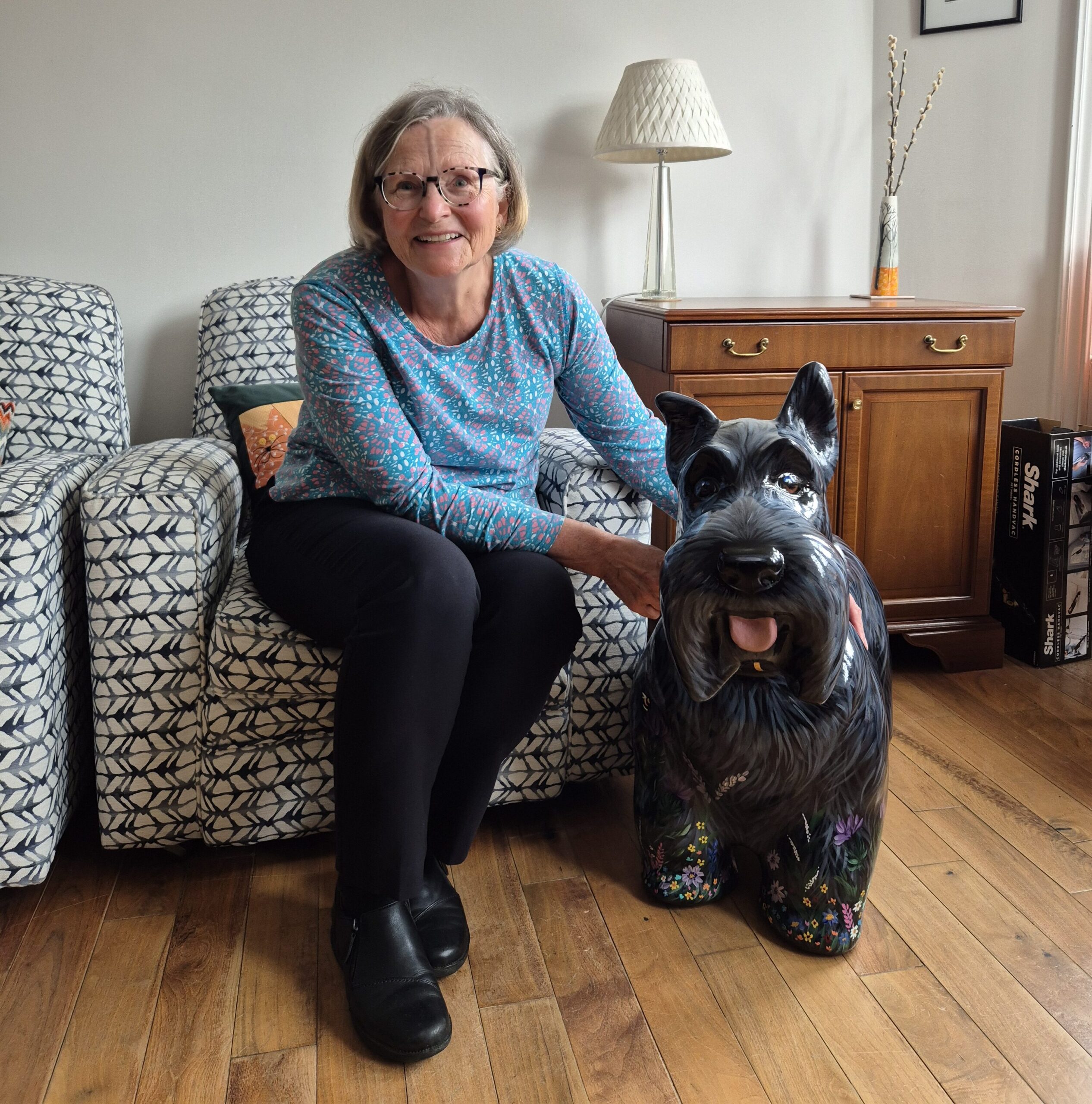 Woman sits next to painted Scottie sculpture, smiling